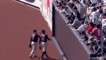 a couple of baseball players are walking on a field while a crowd watches .