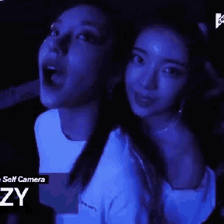 two women are standing next to each other in a dark room with a blue background that says camera zy