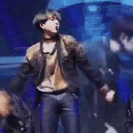 a man in a leather jacket is dancing on a stage in a dark room .