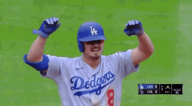 a baseball player wearing a dodgers jersey is standing on the field with his arms in the air .