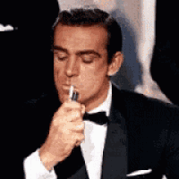 a man in a tuxedo and bow tie is lighting a cigarette .
