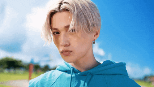 a young man wearing a blue hoodie and earrings looks at the camera