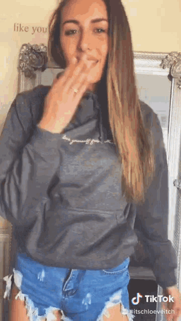 a woman wearing a grey hoodie and shorts is making a funny face .