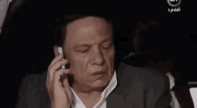 a man in a suit is talking on a cell phone with arabic writing on the bottom right