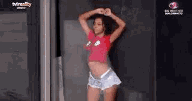 a woman in a red crop top and shorts is dancing in front of a glass door .