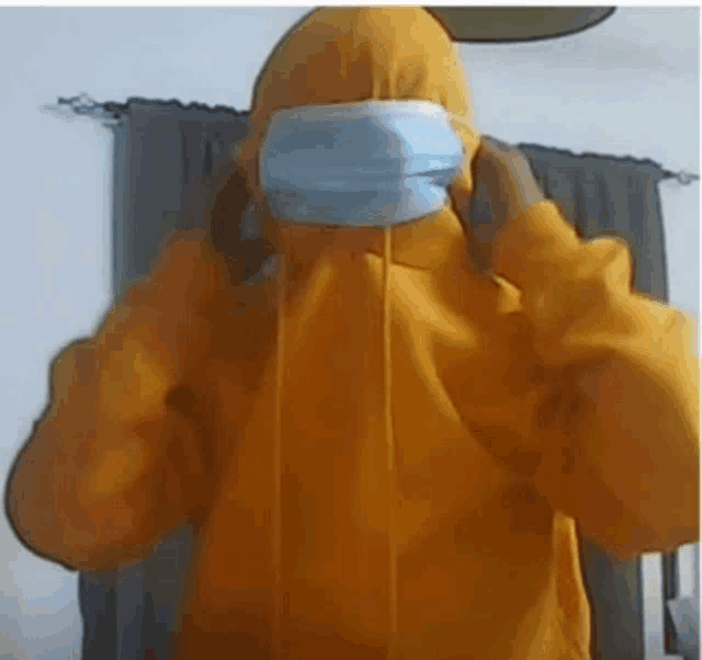 a person wearing a yellow hoodie and a blue mask .