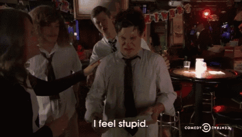 a group of people are standing in a bar and one of them is holding a book and saying " i feel stupid "