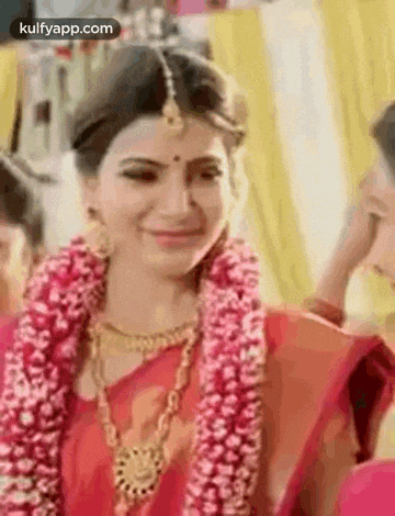 a bride wearing a red saree and a garland of flowers is smiling .
