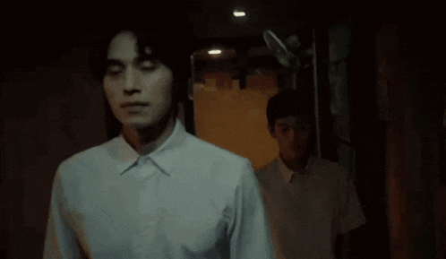 a man in a white shirt is walking down a dark hallway next to another man .