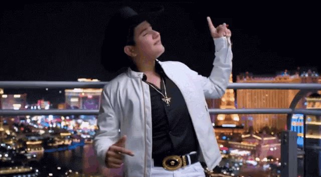 a man wearing a cowboy hat and a white jacket is standing on a balcony giving the thumbs up sign