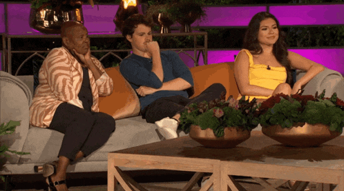 a man and two women sit on a couch with flowers in the background