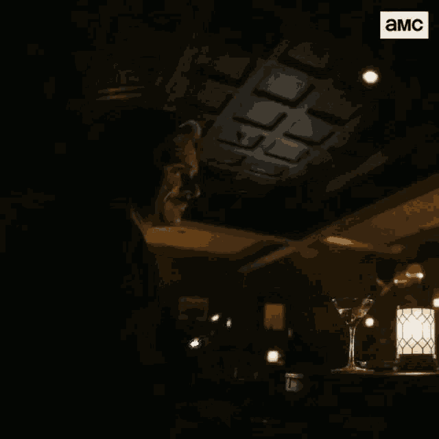 a man is standing in a dark room with a martini glass in front of him .