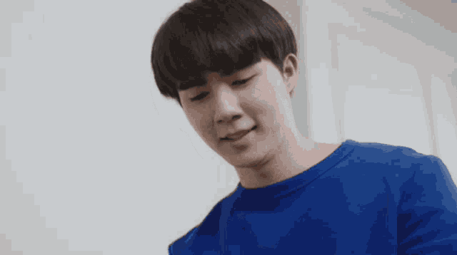a young man wearing a blue sweater is looking down and smiling .