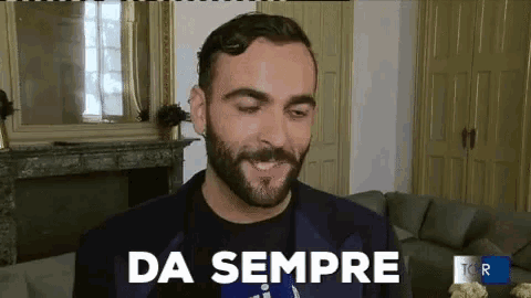 a man with a beard is smiling in front of a fireplace and says " da sempre "