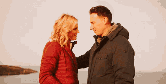 a man and a woman are looking at each other in front of a body of water