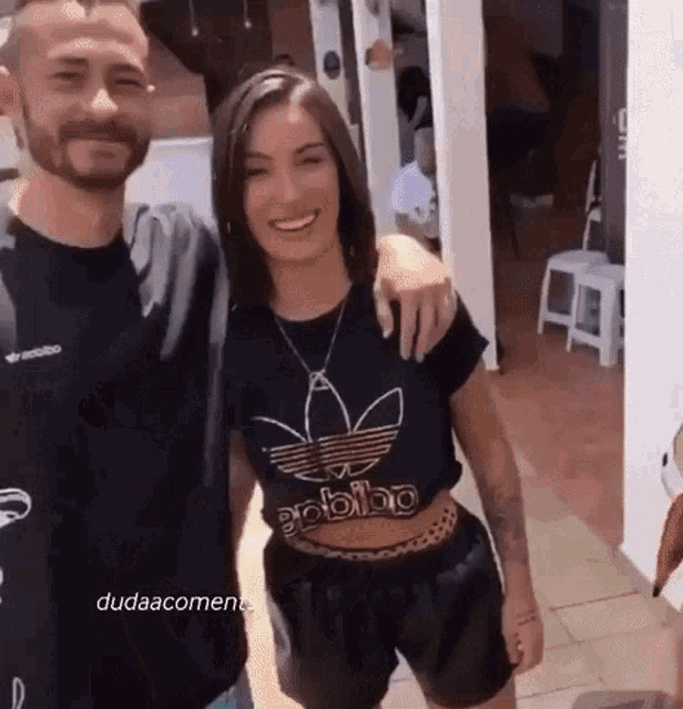 a man and a woman are posing for a picture together . the woman is wearing a black adidas shirt .