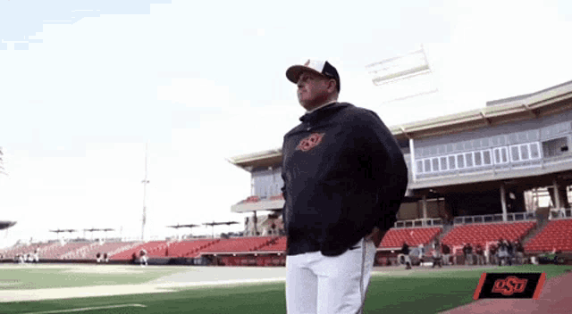 a man stands on a baseball field in front of a stadium that says ost