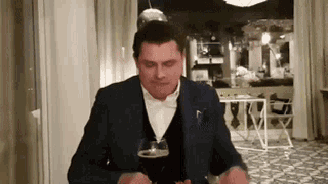 a man in a suit is sitting at a table with a glass of beer in front of him