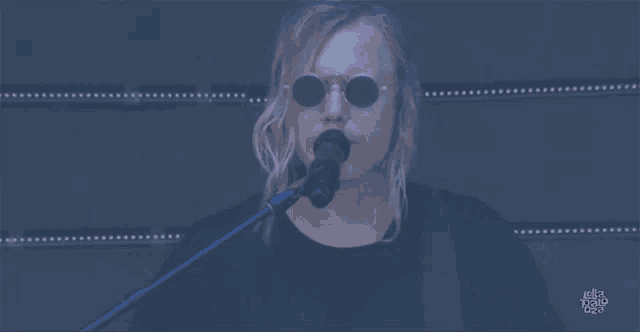 a man wearing sunglasses sings into a microphone in front of a sign that says ' la radio ' on it