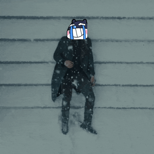 a man in a black coat is standing in the snow with a cartoon face on his head