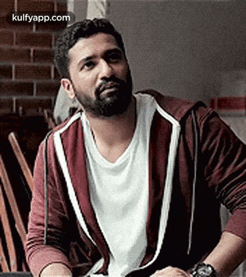 a man with a beard is sitting in a chair wearing a maroon hoodie and a white shirt .