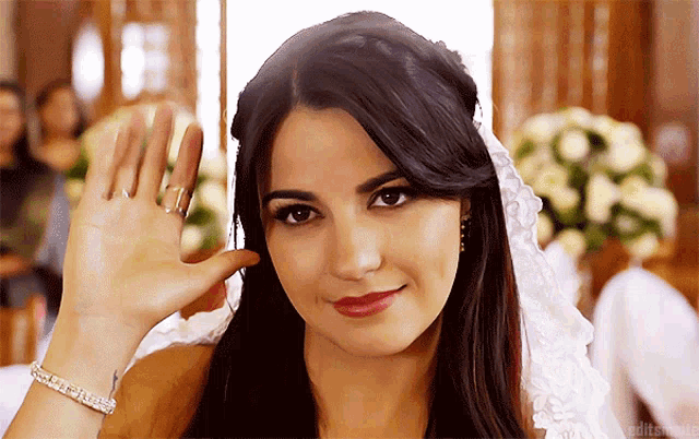 a woman wearing a wedding veil waves her hand