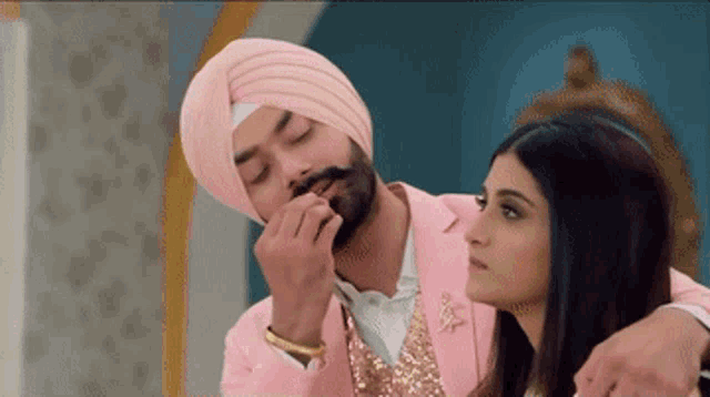 a man wearing a turban and a pink suit looks at a woman