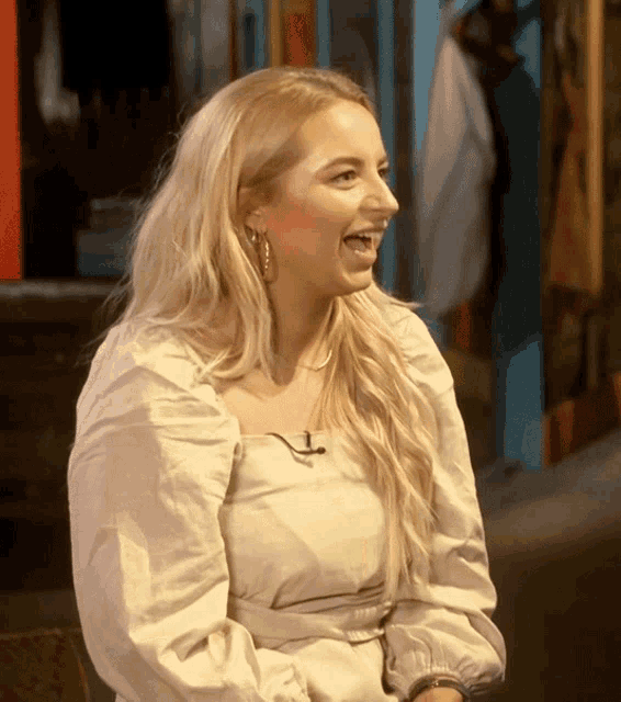 a woman wearing a white top and earrings is smiling