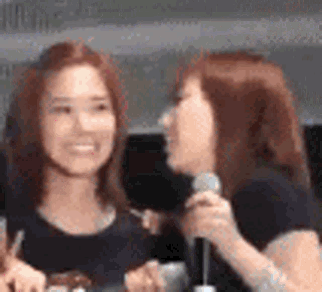 a couple of women are sitting next to each other and one of them is holding a microphone .