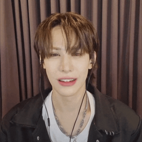 a young man wearing headphones and a necklace looks at the camera with his mouth open