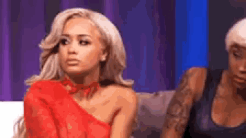 a woman in a red dress is sitting on a couch next to another woman with tattoos .