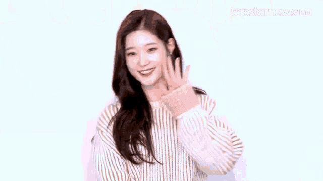 a woman in a sweater is smiling and holding her hair .