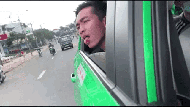 a man sticking his tongue out of a car window while driving down a street .