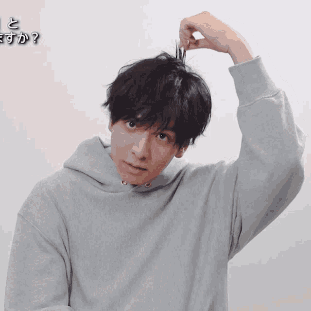 a man wearing a grey hoodie is holding a toothpick in his hair