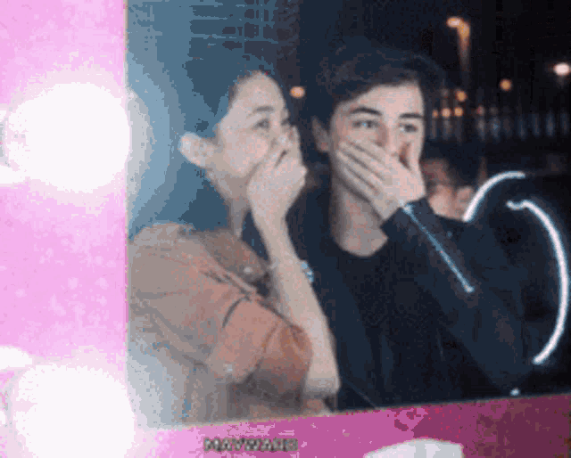 a man and a woman are covering their mouths in front of a mirror that says ' photoflash ' on it