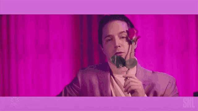 a man in a pink suit is holding a red rose in his mouth ..