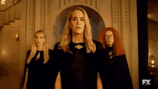 three women are standing next to each other in front of a staircase .