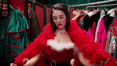 a woman in a santa claus costume is trying on a red feathered cape .