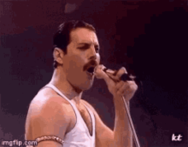 freddie mercury is singing into a microphone while wearing a white tank top .
