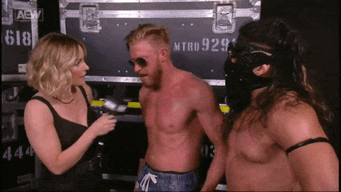 a woman is talking to two wrestlers in front of a case that says aew on it .
