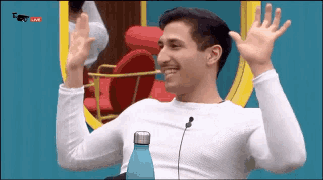 a man in a white shirt is sitting in front of a mirror and waving