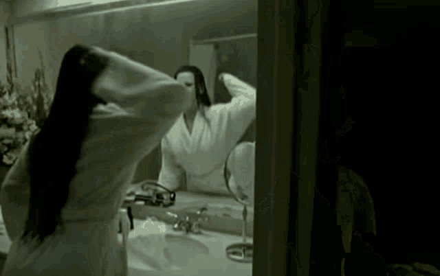 a woman in a bathrobe looks at herself in a mirror