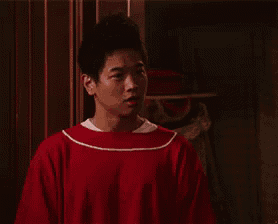 a man in a red sweater is standing in front of a door and giving a thumbs up .