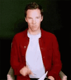 a man wearing a red jacket and a white shirt is sitting in a chair and giving a thumbs up .