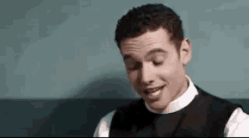 a man in a black vest and white shirt is smiling and looking down .