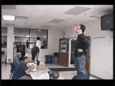 a man in a black shirt is standing in a room with people sitting at tables