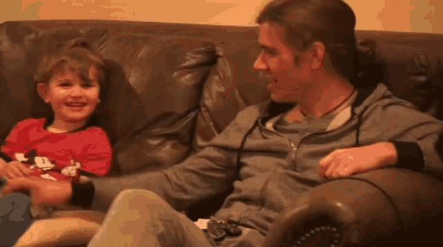 a man and a little girl are sitting on a couch and the little girl is wearing a mickey mouse shirt
