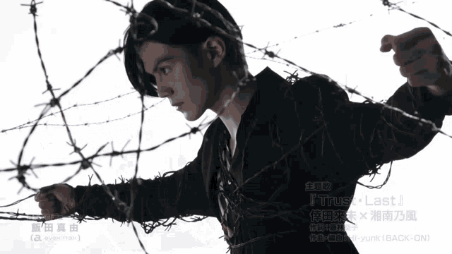 a man with barbed wire around his neck points at the camera