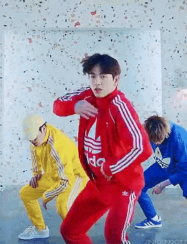 a man in a red adidas jacket is dancing in a room with other men .