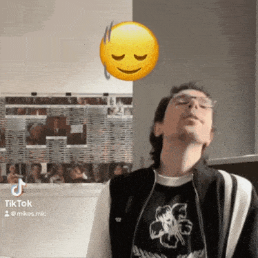 a man wearing glasses and a black shirt with a flower on it stands in front of a wall with pictures on it